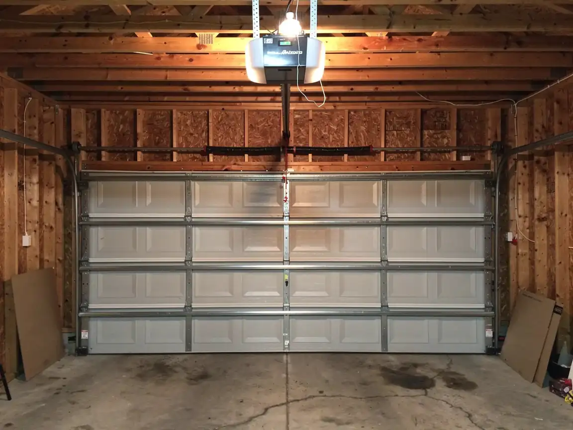 A closed white garage door is visible from inside a garage with wooden walls.