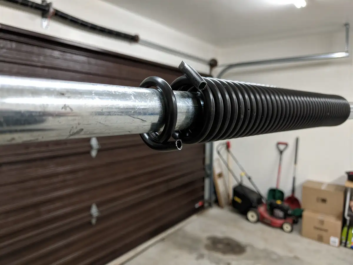 A broken torsion spring is on a metal rod above a brown garage door.